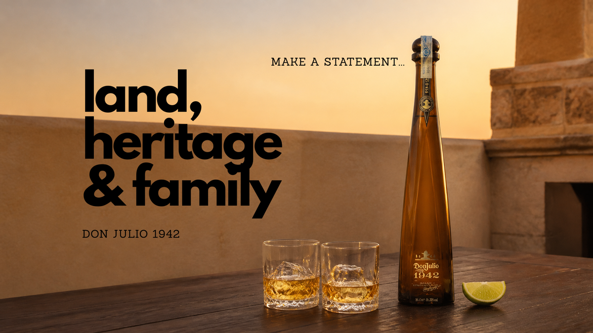 A bottle of Don Julio 1942 tequila and two rocks glasses filled with the golden liquid, set on a wooden table against a warm sunset background with architectural stone details. Large text on the left reads 'land, heritage & family' with smaller text 'DON JULIO 1942' and 'MAKE A STATEMENT.